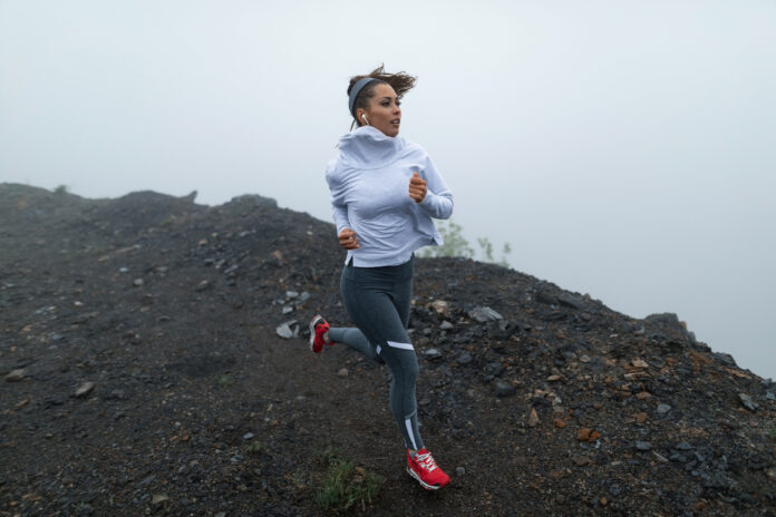 Young athletic woman running on a cliff against foggy sky.